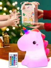 Unicorn-shaped night light with remote control, gift box, and hands reaching towards it on a festive background.